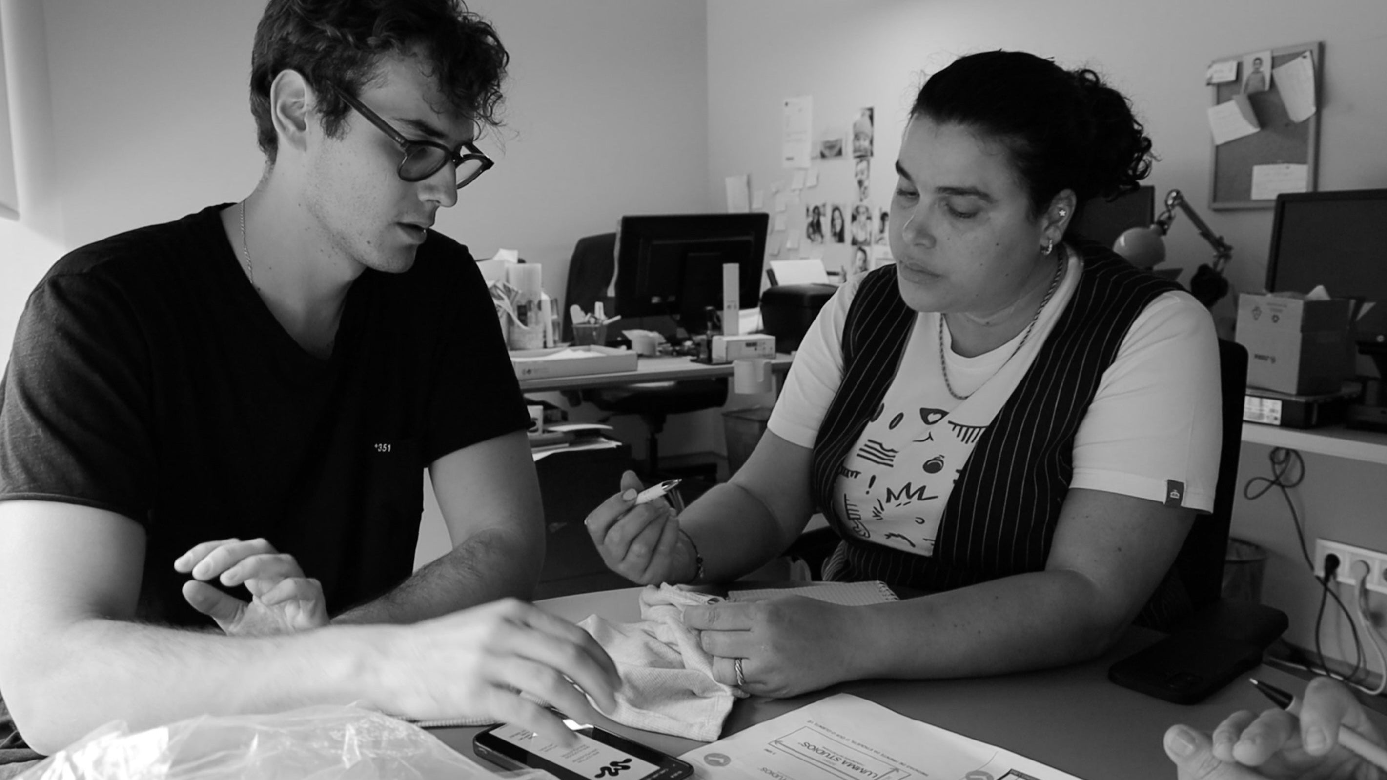 Two people sitting at a desk in an office setting, engaged in a discussion.