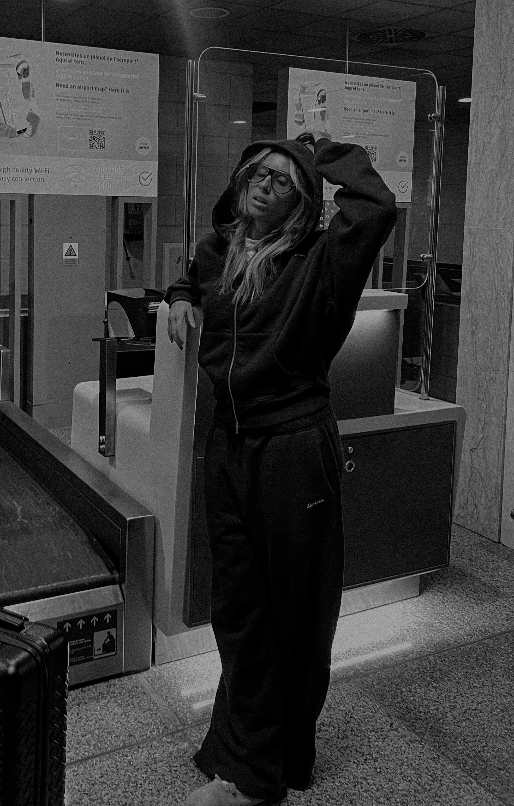 Person standing in a public space with a counter and signs in the background