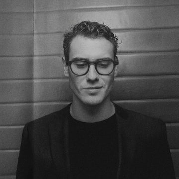 Black and white portrait of a person wearing glasses against a textured wall.