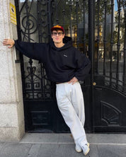 Person wearing a black hoodie and white pants leaning against a decorative metal gate.