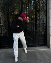Person wearing a red cap and white pants standing in front of an ornate metal door.