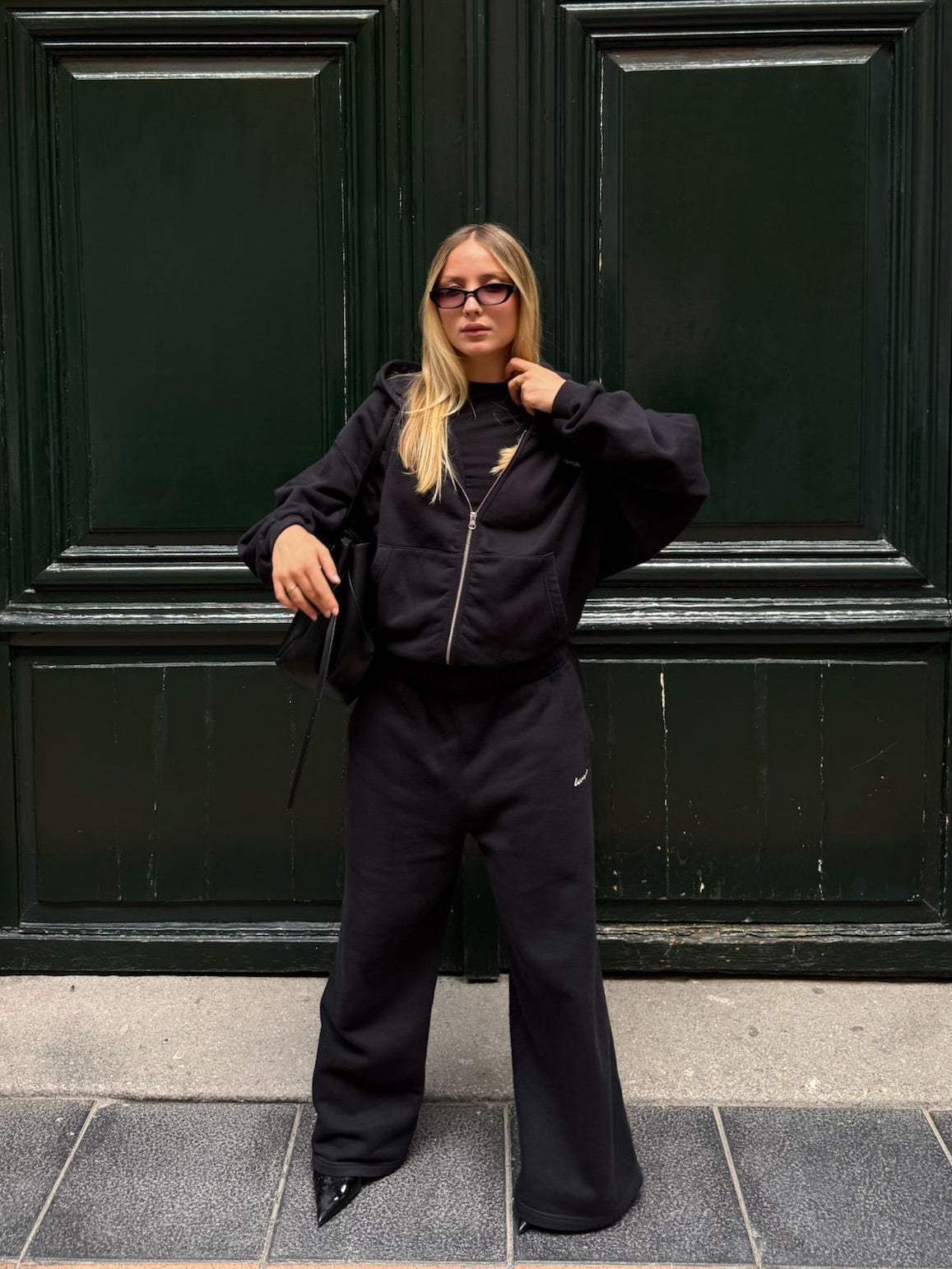 Person wearing a black outfit standing in front of a large black door.